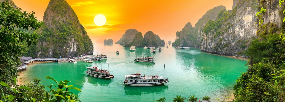 cruise boats in ha long bay vietnam with limestone cliffs and turquoise waters at sunset