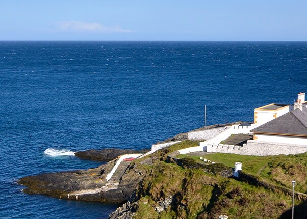 a white lighthouse is located a hillside