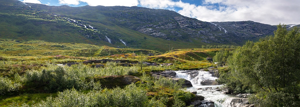 a waterfall and stream with the mountains in the background in haugesund, norway
