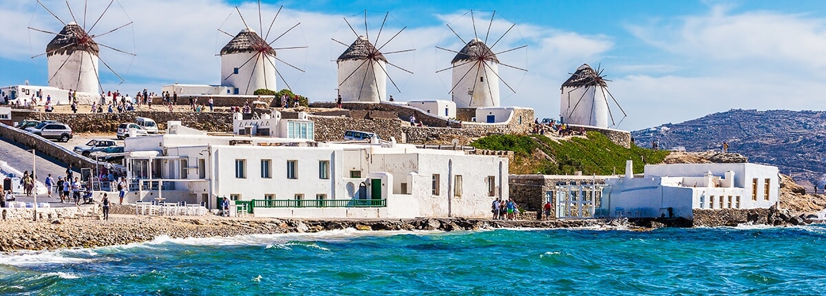 windmills lining mykonos streets with beautiful teal waters