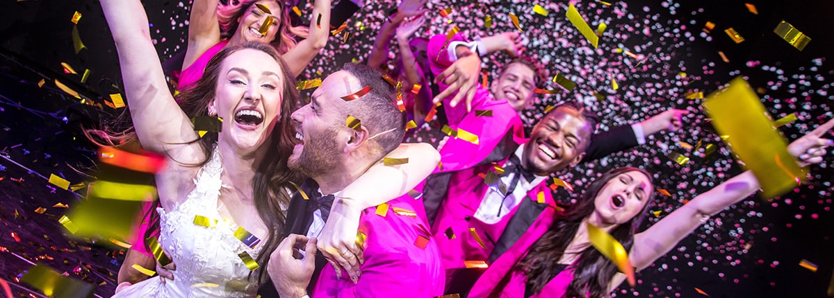 a group of actors in pink tuxedos and dresses celebrating with confetti 