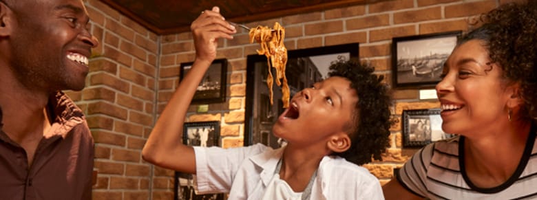 father and mother happily watch as son eats spaghetti at carnival's cucina del capitano