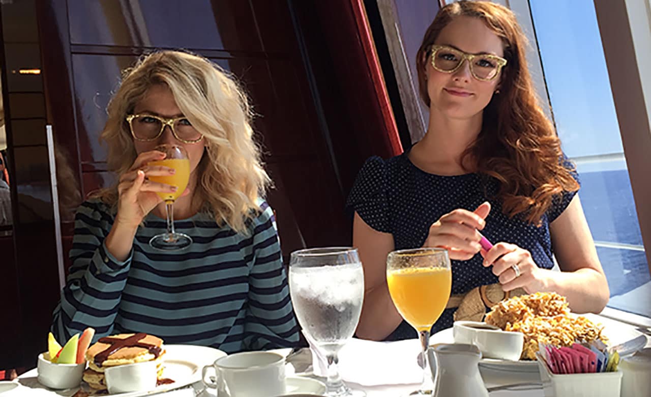 Two women sitting for breakfast at restaurant table on carnival ship, one drinking her beverage