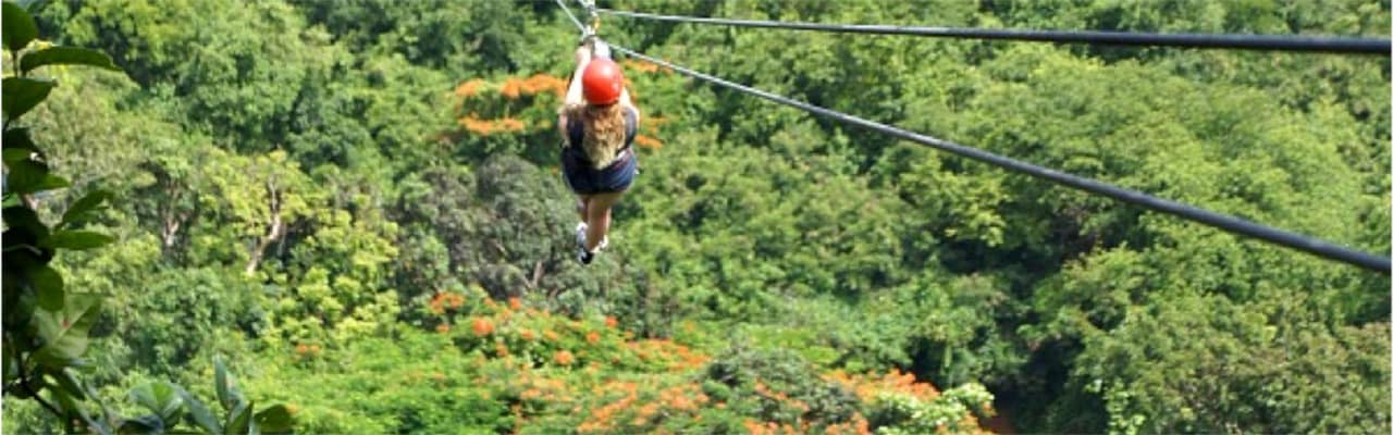 Woman riding across zip line over wooded area, wearing red helmet