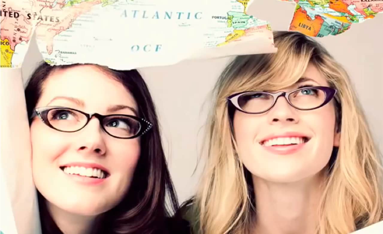 Two girls wearing glasses look up to a semi-torn map of the world