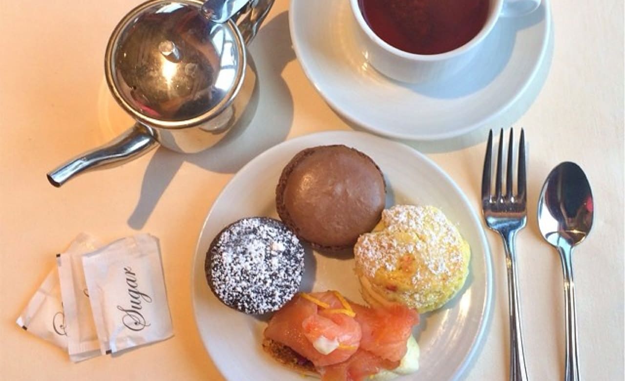 Place setting with a plate of desserts, a teacup, small tea kettle, packets of sugar and silverware