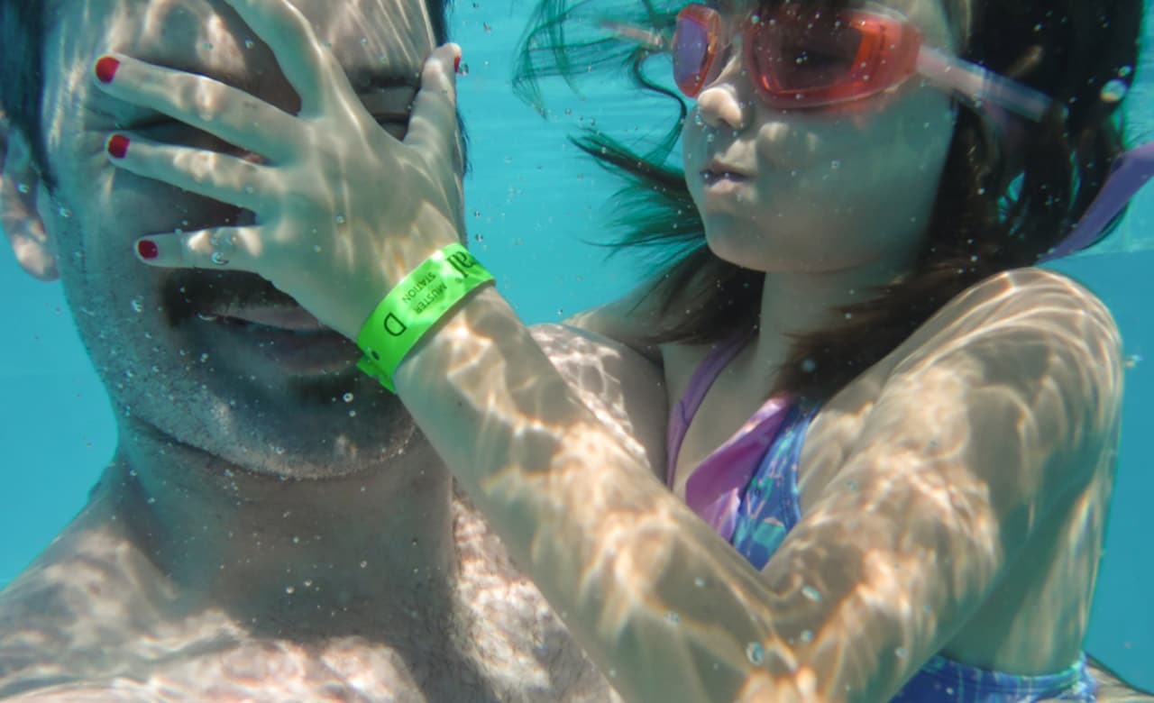 Underwater, a man holds female child wearing goggles and covers his face with her hand