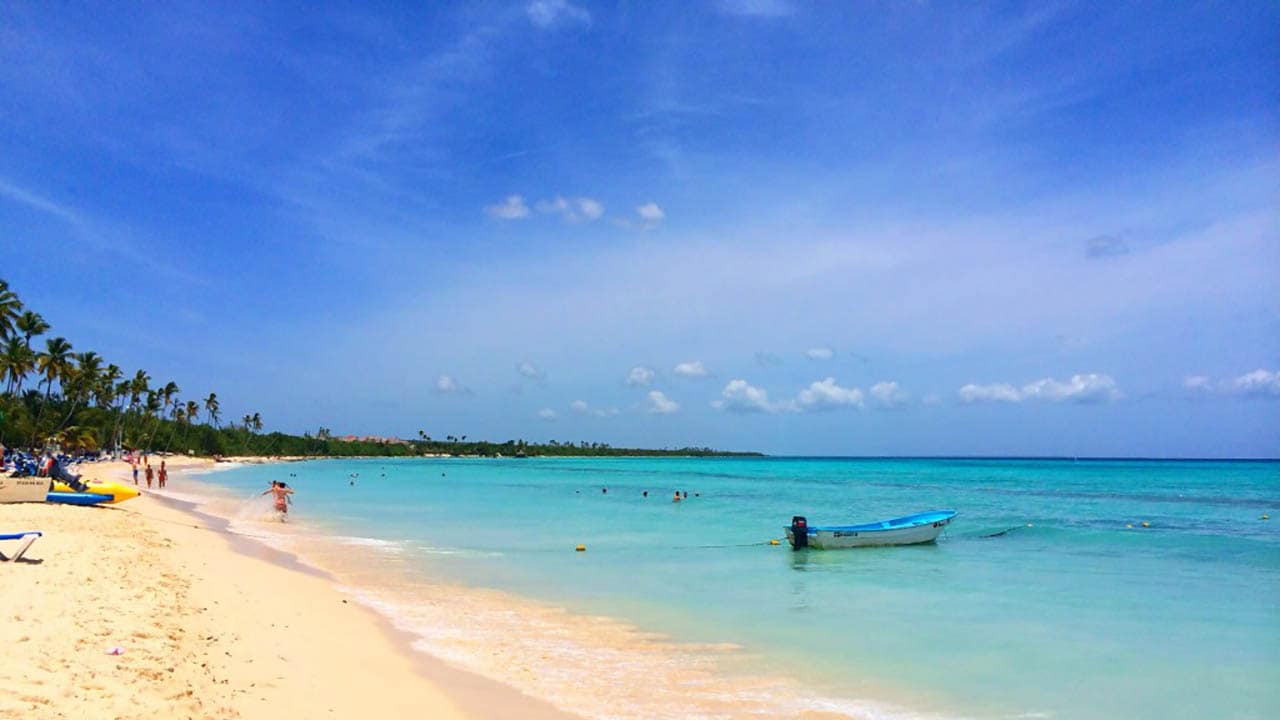A small motor boat anchored near a beach as people in the distance play and swim