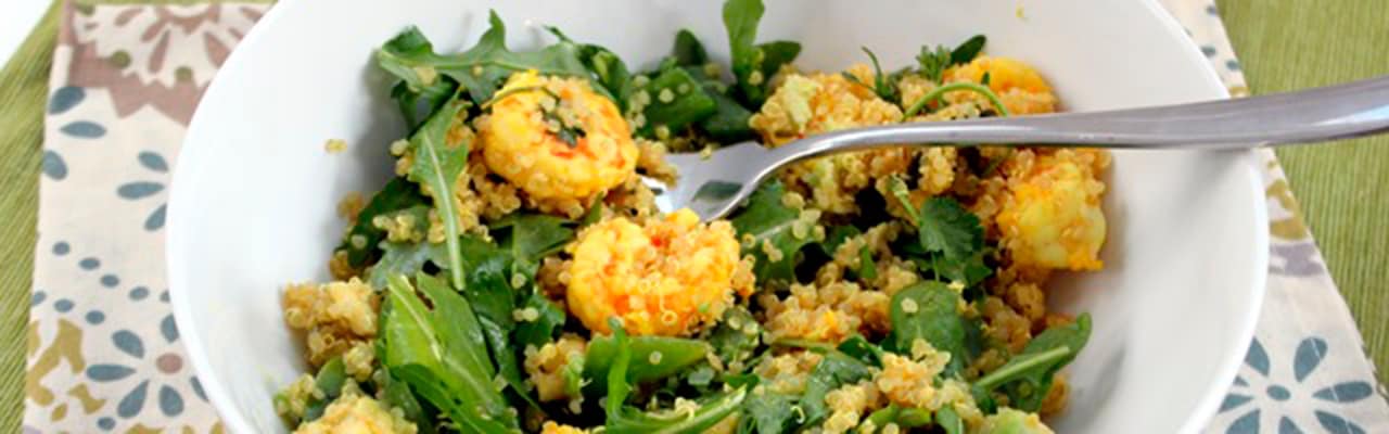 A white bowl filled with arugula greens, quinoa and shrimp poked with metal fork