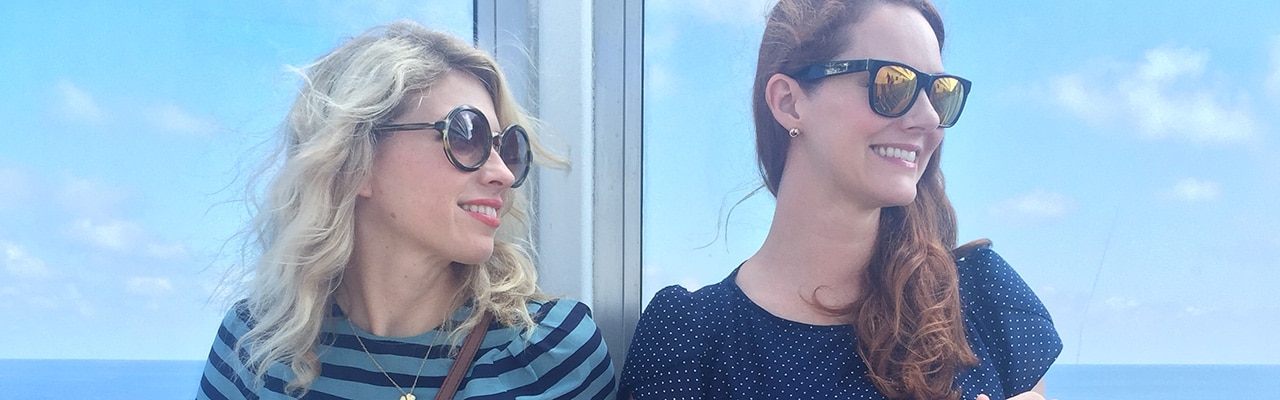 Two women stand next to a glass wall, looking to their side