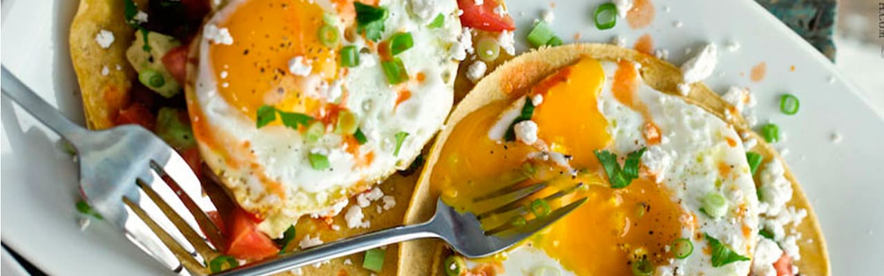 Two forks resting on plate of eggs, tortillas, and chives – one egg yolk has been broken