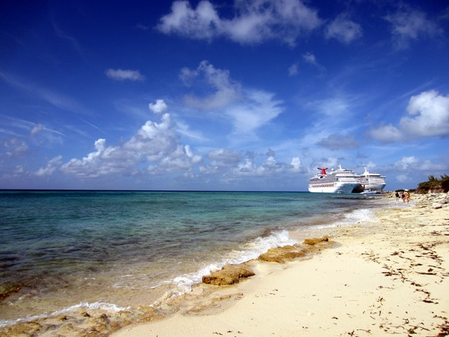 Two carnival cruise ships docked parallel to each other in the distant background of an empty beach