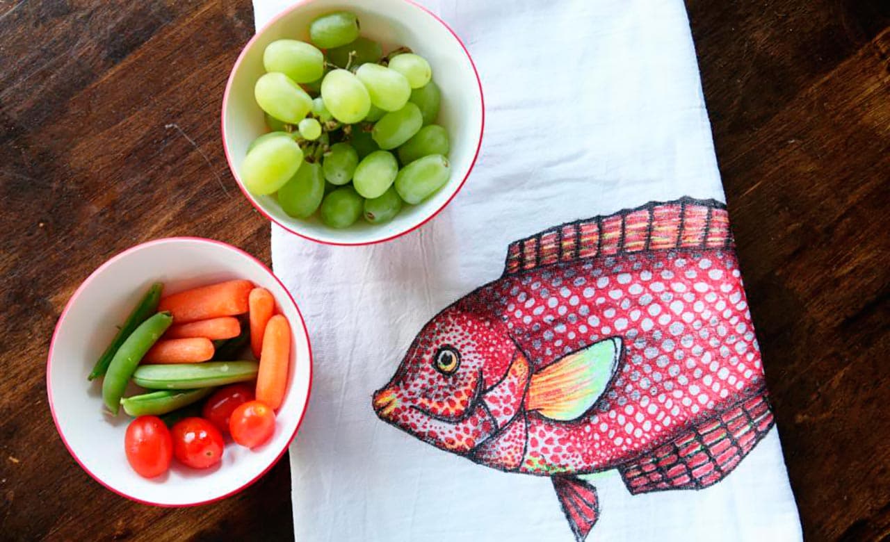 A fish-printed towel rests under two small bowls filled with grapes and vegetables