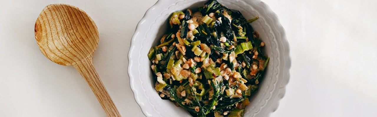 Bowl filled with greens, grains and nuts placed next to a large wooden spoon