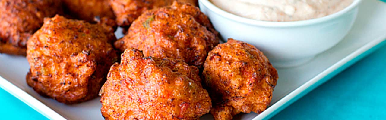 Plate of ball-shaped fried food next to a bowl of a white dipping sause