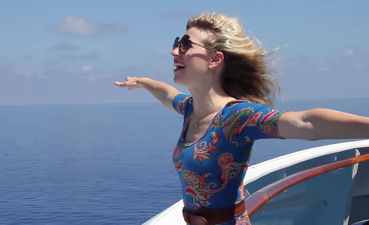 A woman laughs as she opens her arms at bow of ship