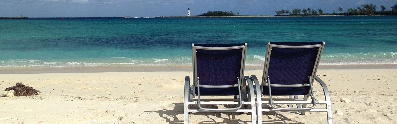 Two beach chairs over look the ocean and a lighthouse in the distance in the caribbean