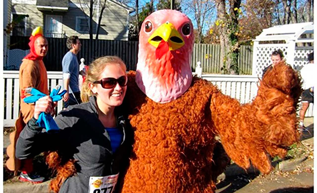 Person wearing a turkey costume poses with woman in running gear on a street