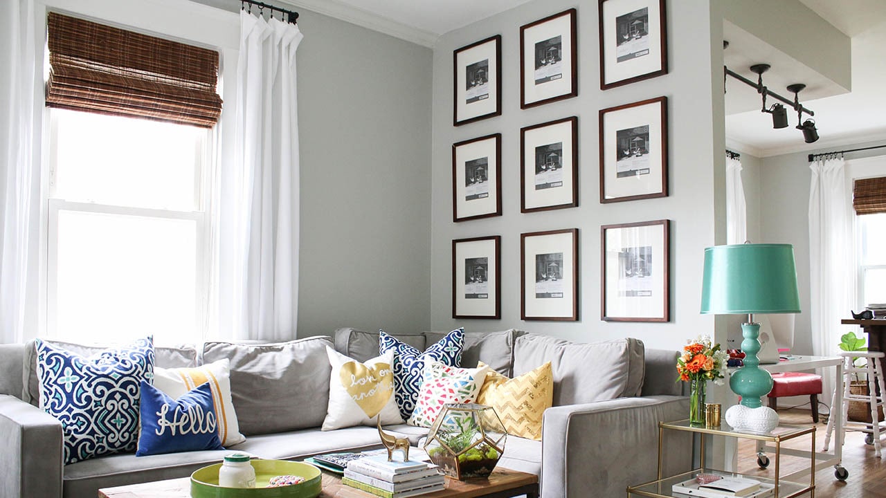 Living room interior with grey walls, couch, colorful pillows and nine pictures hanging on dividing wall