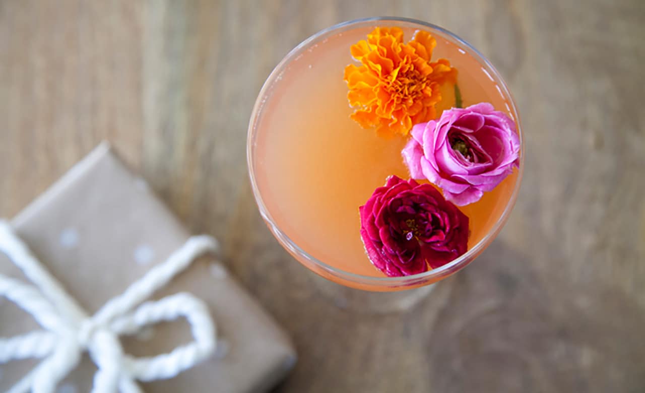 looking into a glass filled with an orange cocktail and three small flower garnishes