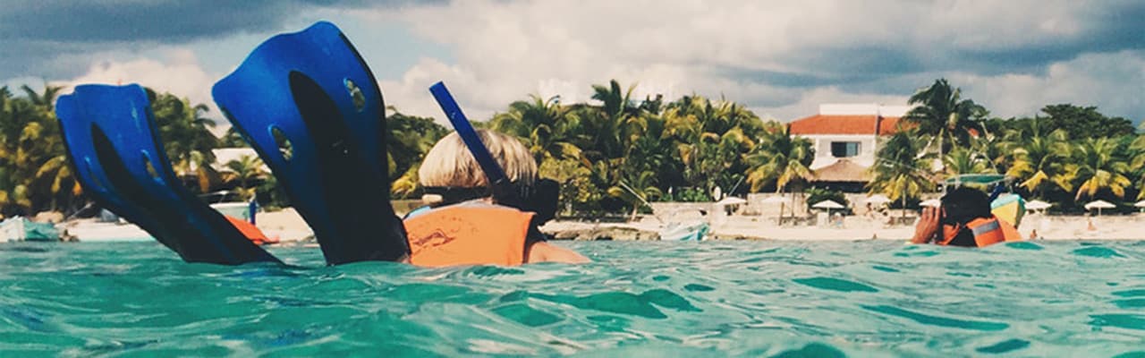 Two people snorkeling, fins are in the air as one catches up to the other