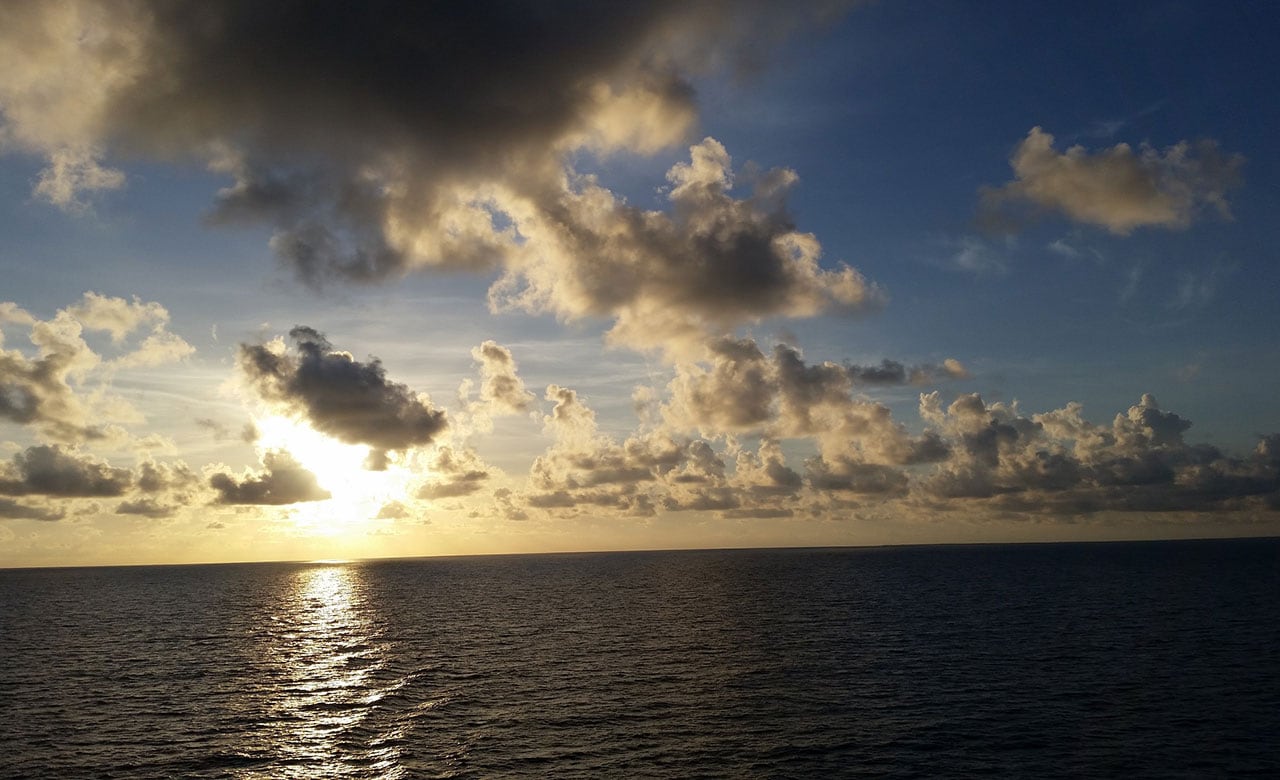 The sun beginning to set behind clouds over the ocean