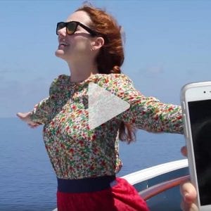 girl with glasses stands on ship with arms outstretch posing for photo, link to Youtube video