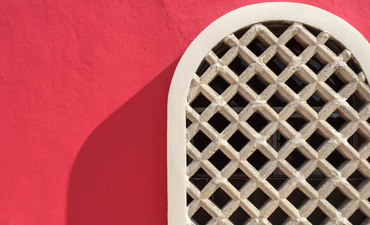 Sun shining on red clay wall with white arched window