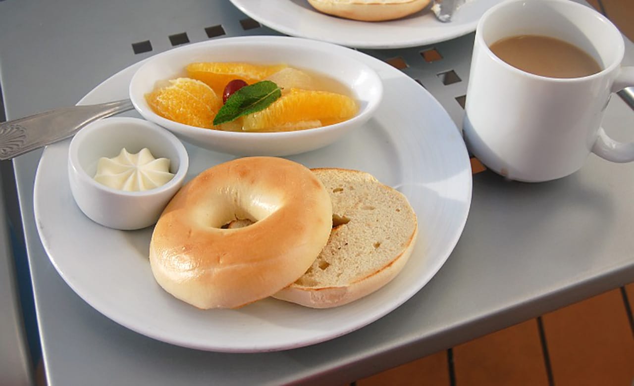 Breakfast plate of a bagel, butter, and sliced oranges lay next to a cup of coffee