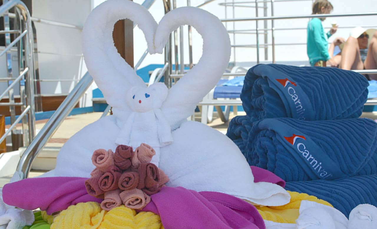 White towels formed into swans and a bear next to blue carnival-branded towels on ship