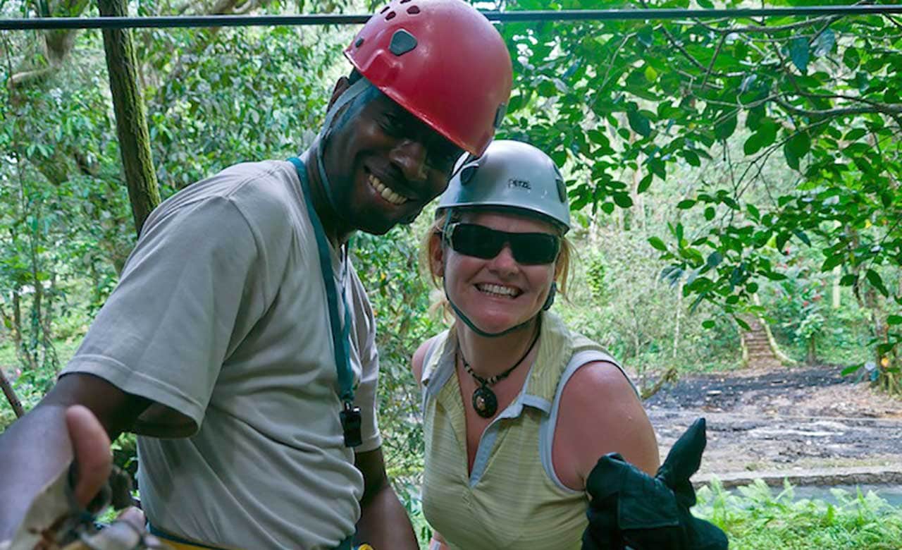 Man in red helmet and woman in blue helmet smile in a wooded area