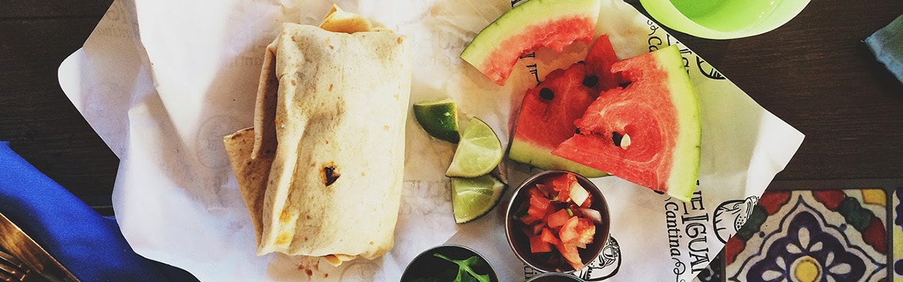 A burrito from blue iguana cantina with limes and slices of eaten watermelon