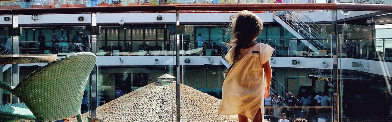 Small girl faces a glass wall overlooking crowd of people on the ship's pool deck
