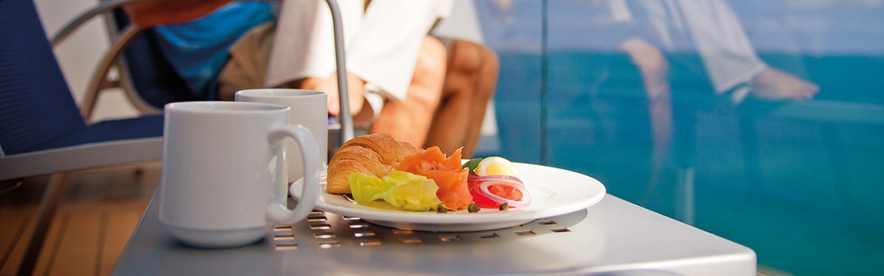 Plate of breakfast and two cups sit next to a couple enjoying a balcony