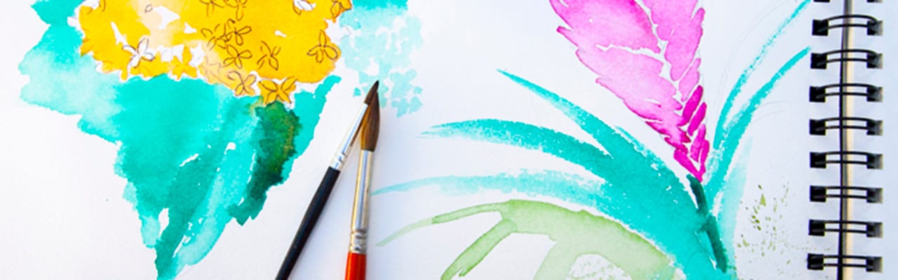 Two paint brushes sit on a pad of paper painted on with a floral images