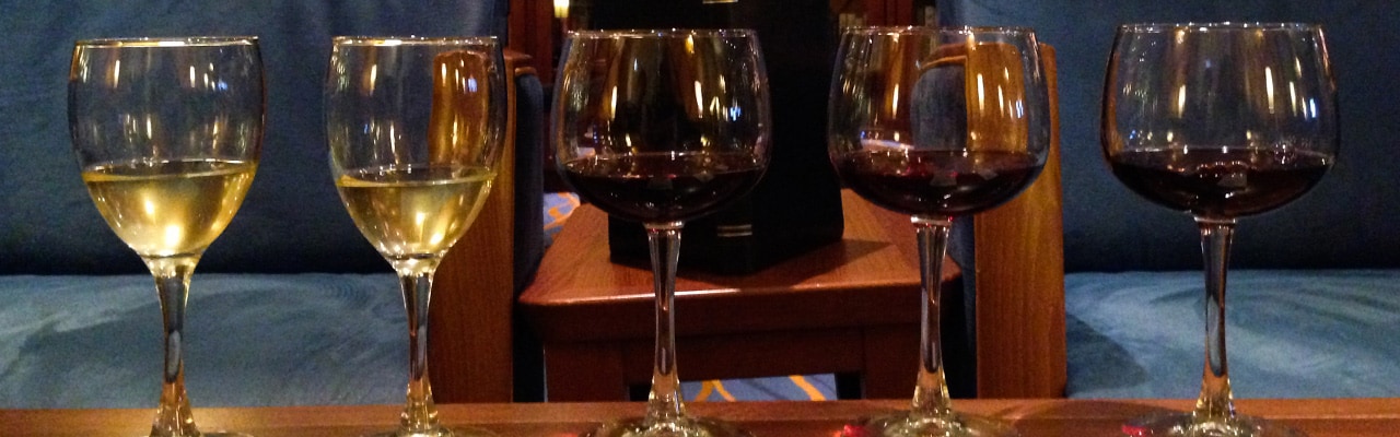 Two glasses of white wine and three glasses of red sit on a wooden table