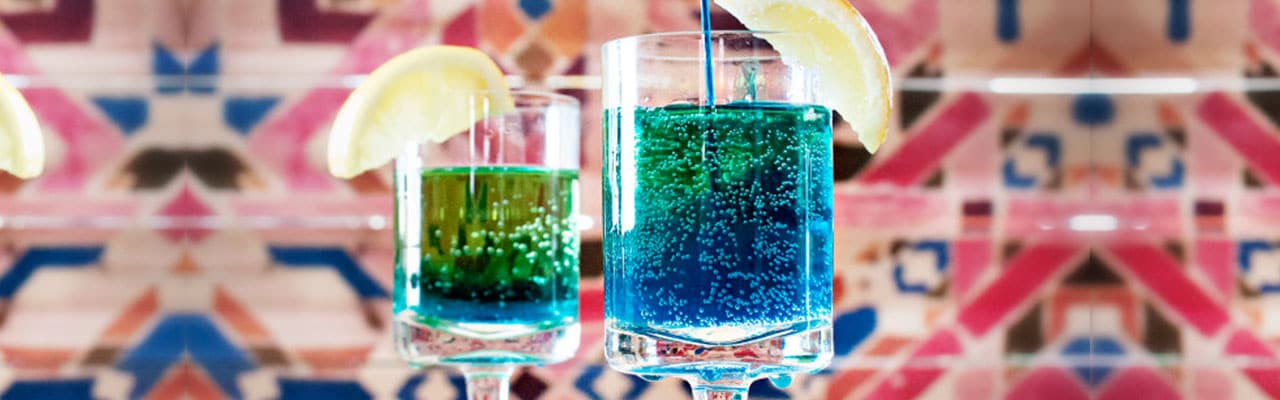 A blue liquid is poured into a glass with lemon garnish