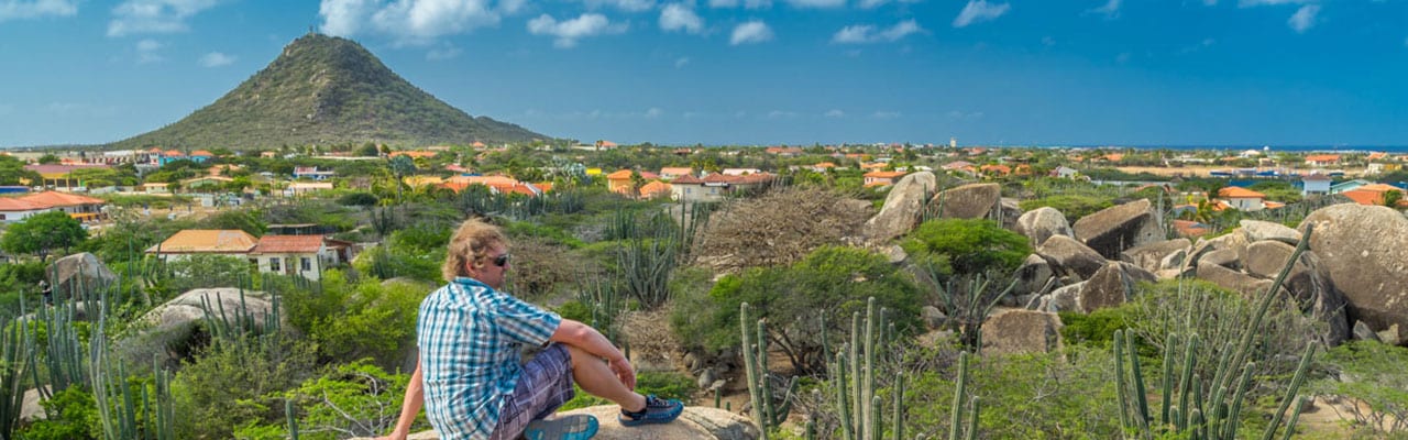 Man sitting on cliff looking over village with vulcano