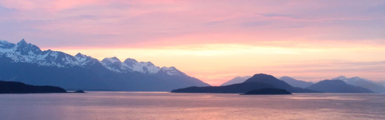 Sun setting over snow capped mountains at sea