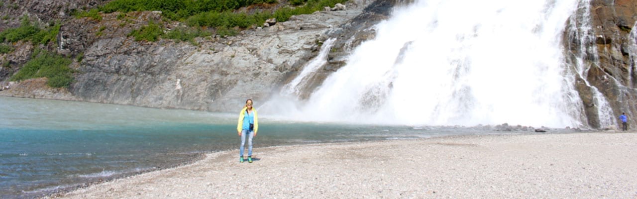 Woman standing next to large waterfall in Alaska