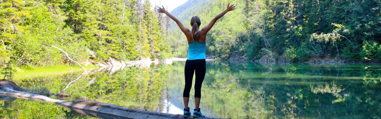 Woman standing with her arms in the air on a log in a steam in alaska