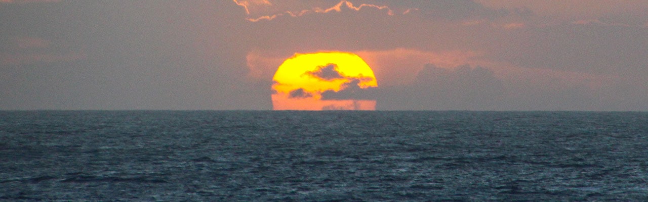 Orb of sun falling into the ocean horizon line
