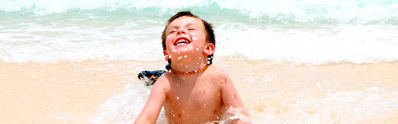 Boy laughs as he lays in sand, waves crashing into him
