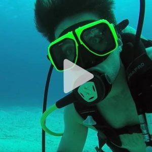 Man scuba diving with goggles on looking at the camera, link to YouTube video
