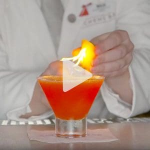 cocktail being made with an on fire fruit garnish by a Carnival mixologist, link to Youtube video