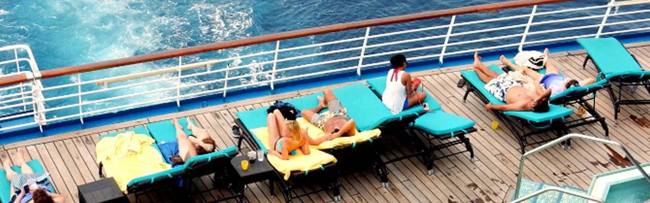 people relaxing on lounge chairs on carnival ship deck with water in background