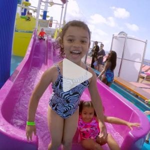 little girl smiles as she gets up from water slide on a Carnival ship, link to Youtube video
