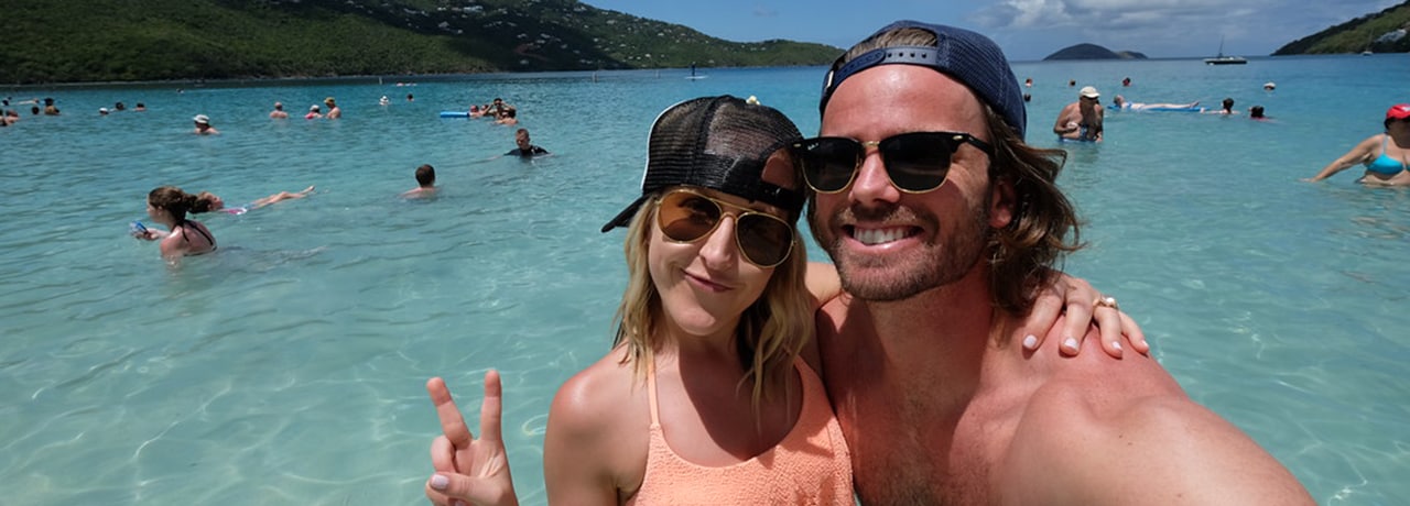 Banner image of a male and female smiling in front of a beach on Magens Bay