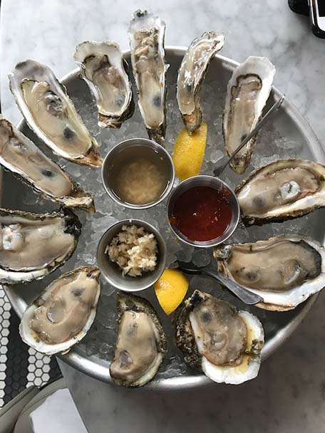 Overhead image of a dozen oysters over ice with three sauces