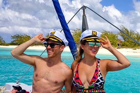 Jeremy and friend wearing captain hats with the blue caribbean ocean and white sand beach behind them